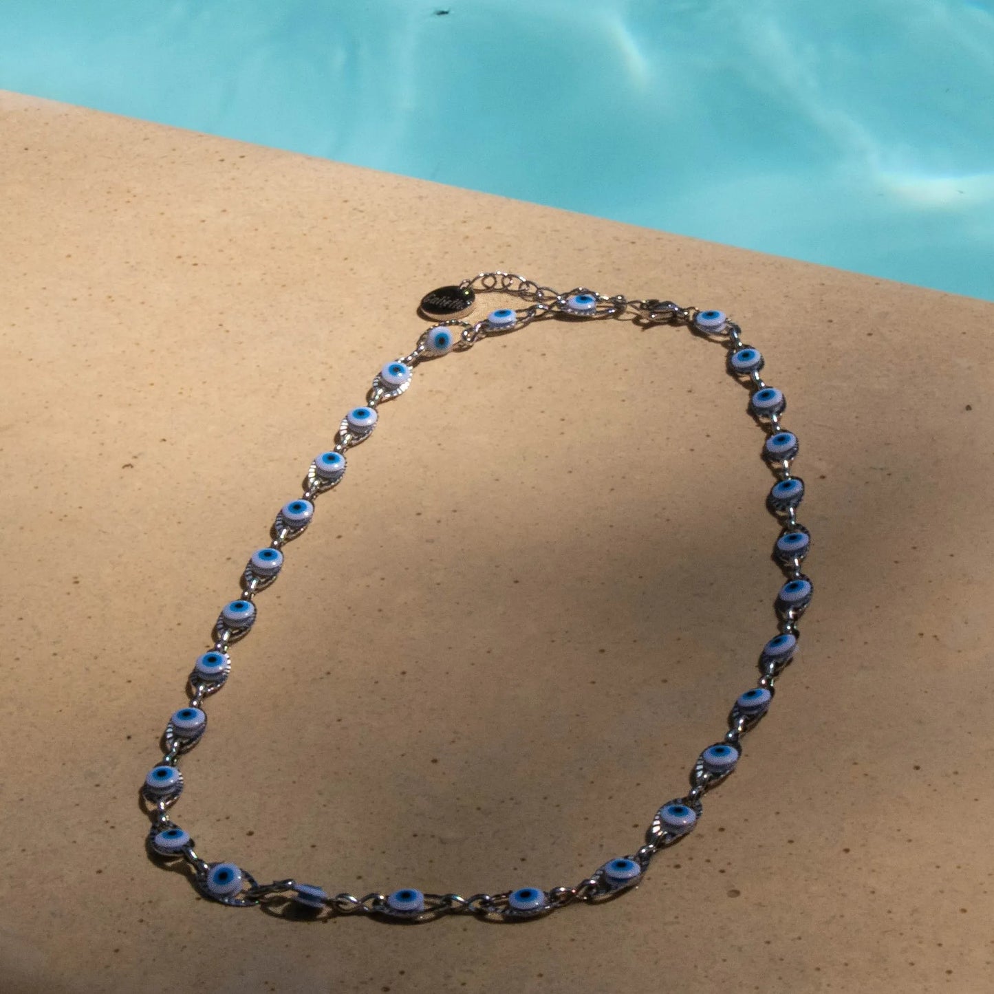 Collier femme en acier inoxydable, perles blanc, bleu clair et bleu, bijou élégant et résistant. Posé au bord d'une piscine