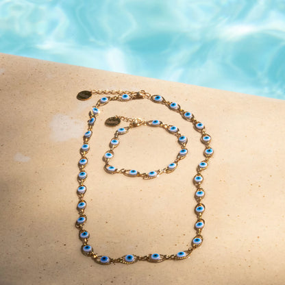 Parure contenant bracelet et collier femme en acier inoxydable doré, époxy blanc, bleu clair et bleu, bijou élégant et résistant. Posé au bord d'une piscine